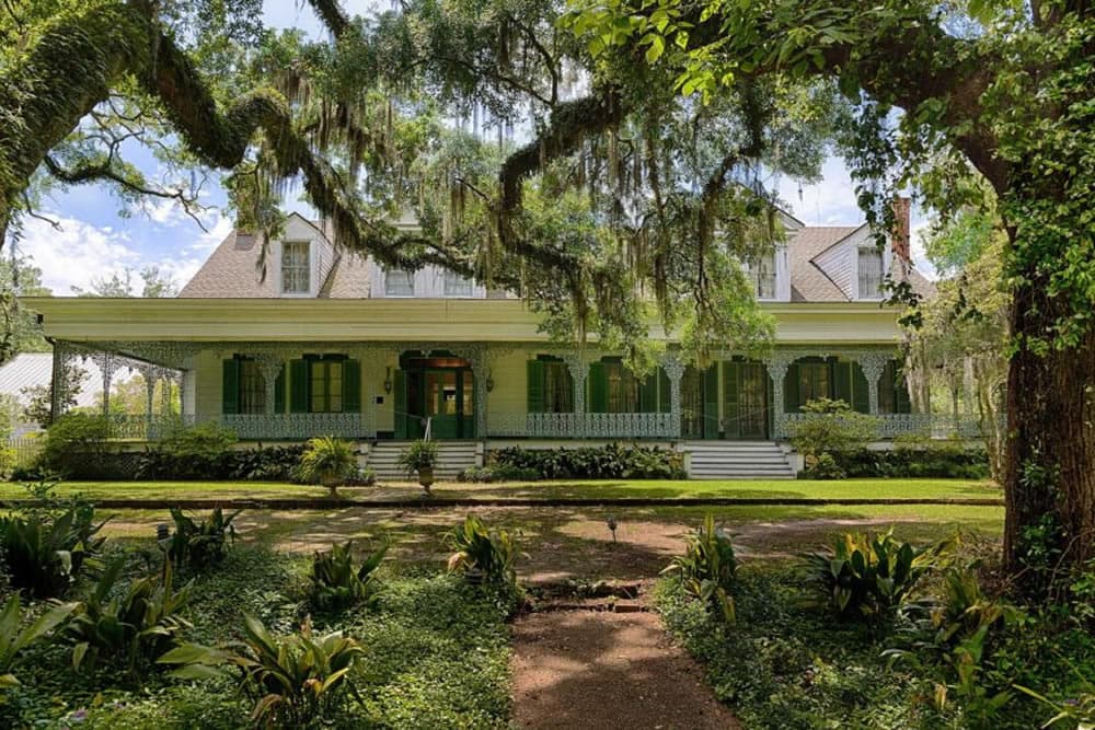 A picturesque southern-style house surrounded by lush greenery and Spanish moss.