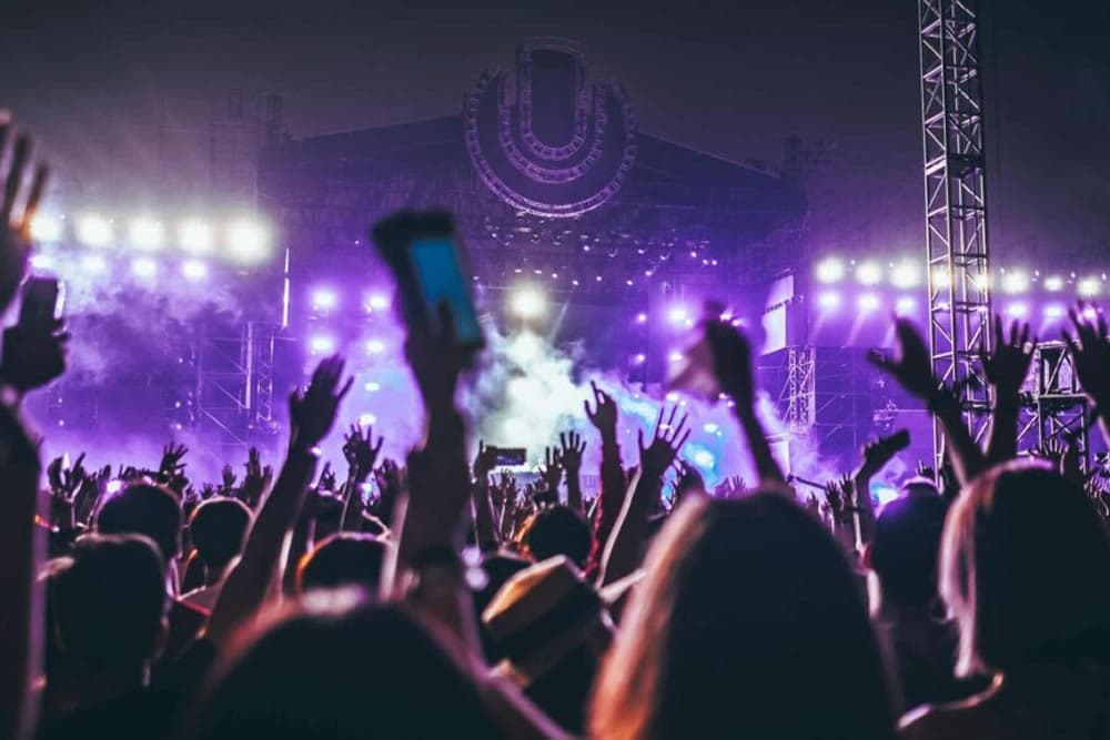 A crowd raises their hands in excitement at a vibrant music festival stage.