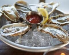 Plate of oysters on ice with a lemon wedge and cocktail sauce.