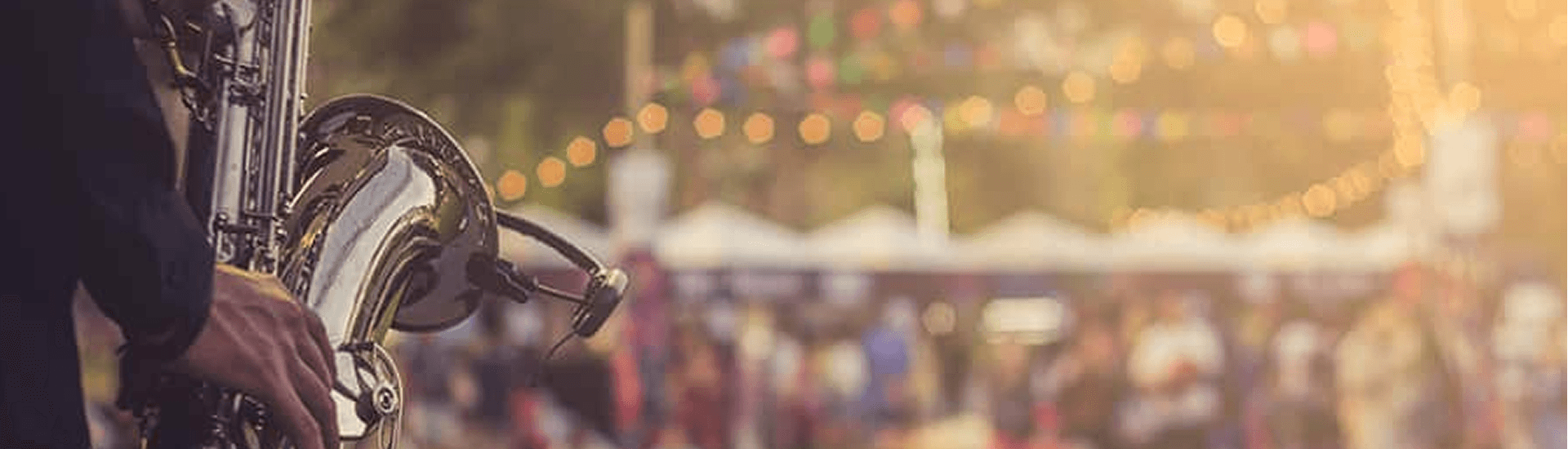 A close-up of a saxophone being played at a lively outdoor festival with festive lighting in the background.