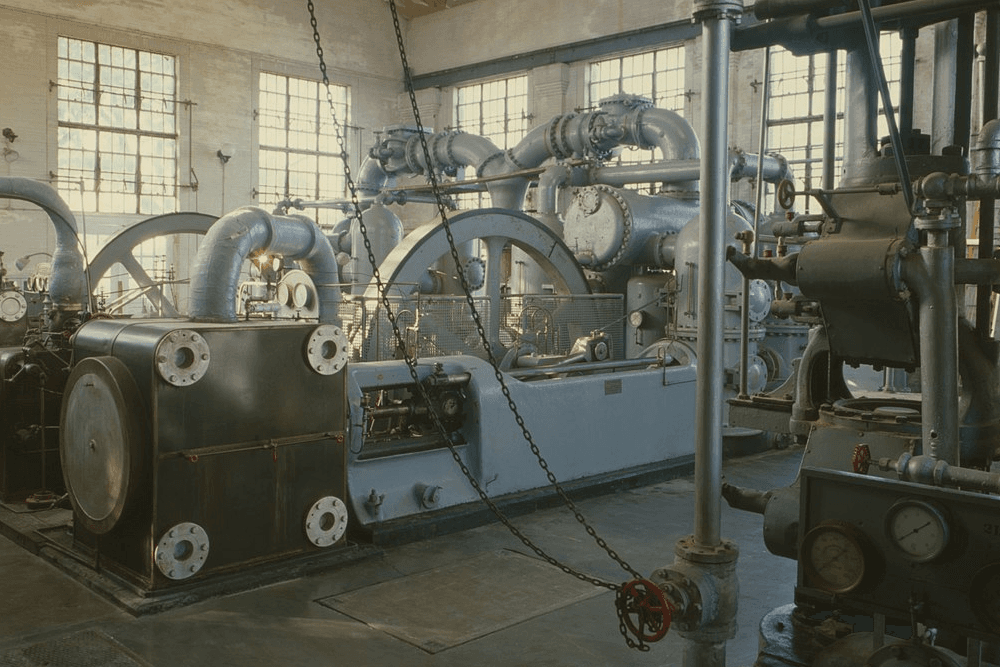 Industrial machinery with large pipes and gears in a well-lit factory space.