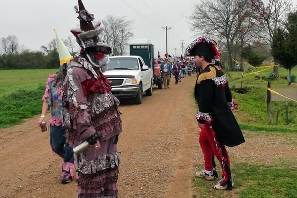 A colorful parade with participants in elaborate costumes walking along a dirt road.
