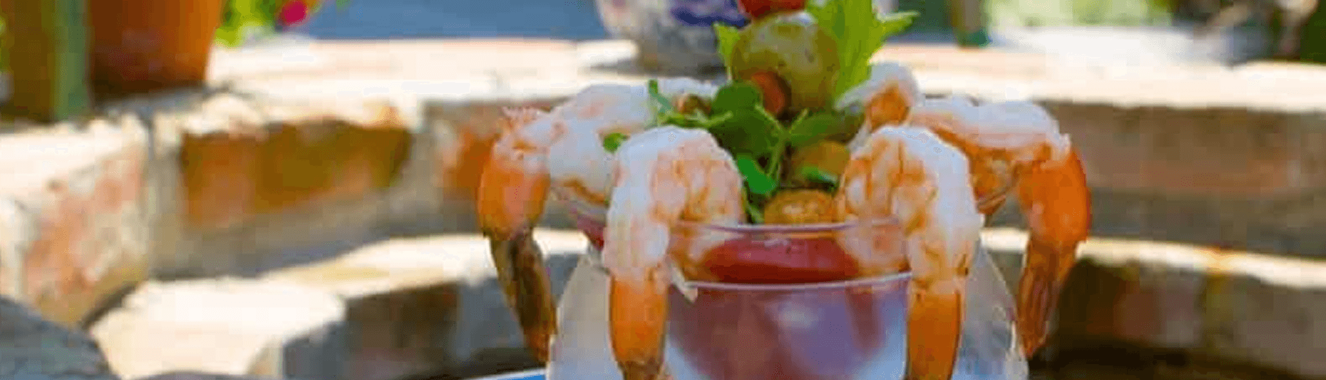 A shrimp cocktail garnished with olives and greens served in a glass.