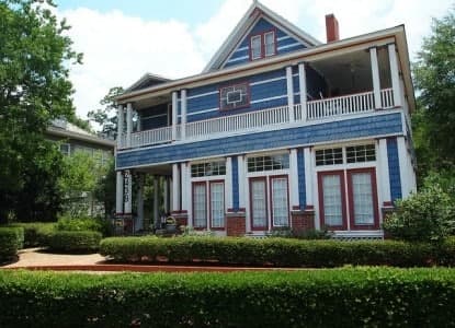 A large blue and white Victorian-style house with a porch and landscaped front yard.