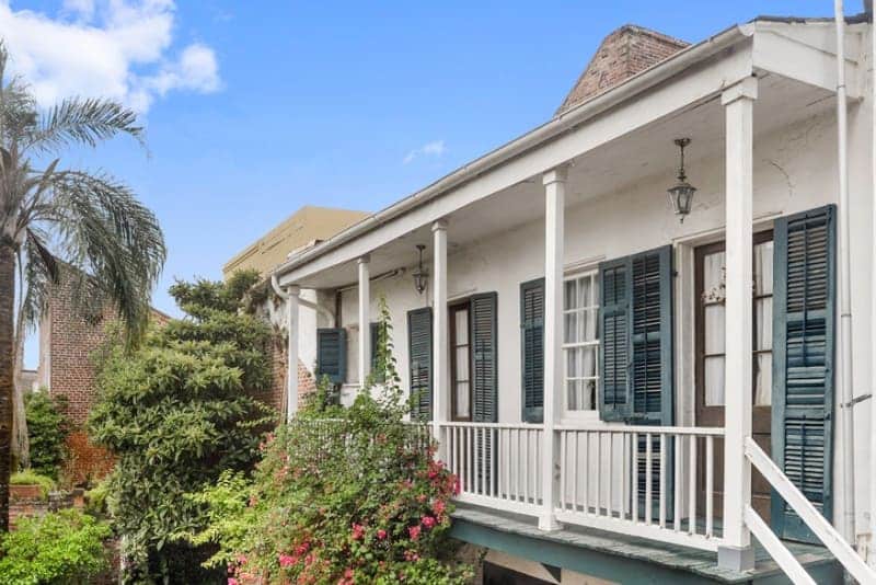 A historic house with a porch surrounded by lush greenery and blue skies.
