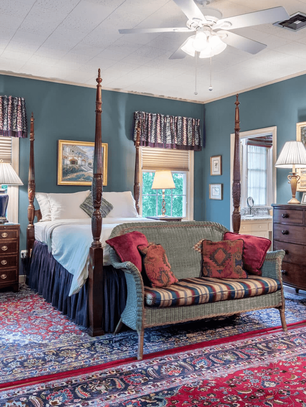 A cozy bedroom featuring a four-poster bed, vintage furnishings, a patterned rug, and warm lighting.