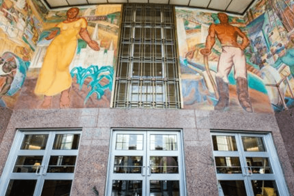 Mural depicting a woman in a yellow dress and a man in work attire, located above entrance doors.