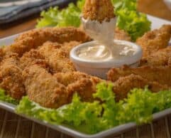 A platter of crispy fried chicken tenders surrounded by lettuce and served with a dipping sauce.