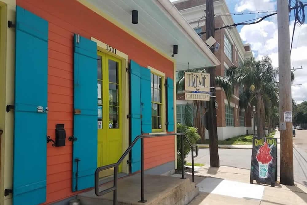 Colorful coffeehouse exterior with teal shutters and a bright yellow door, featuring a sign and sidewalk chalkboard.