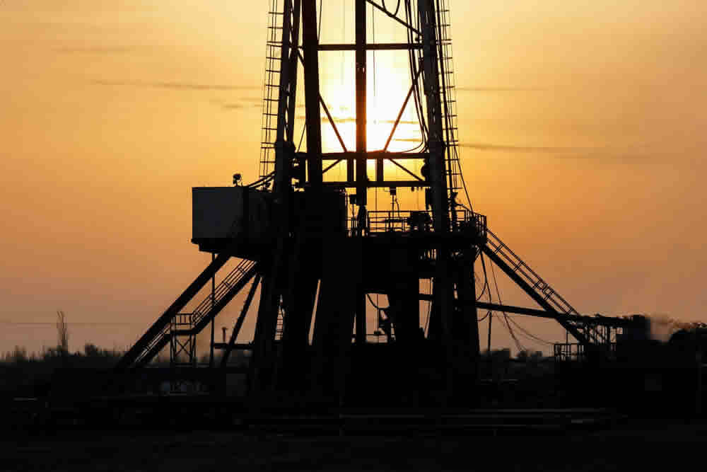 Silhouette of an oil rig against a sunset sky.