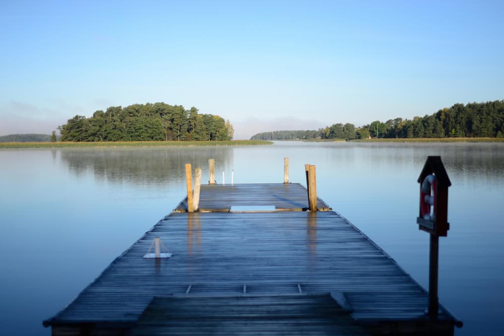 A wooden dock extending over a calm lake with a backdrop of trees and a blue sky.