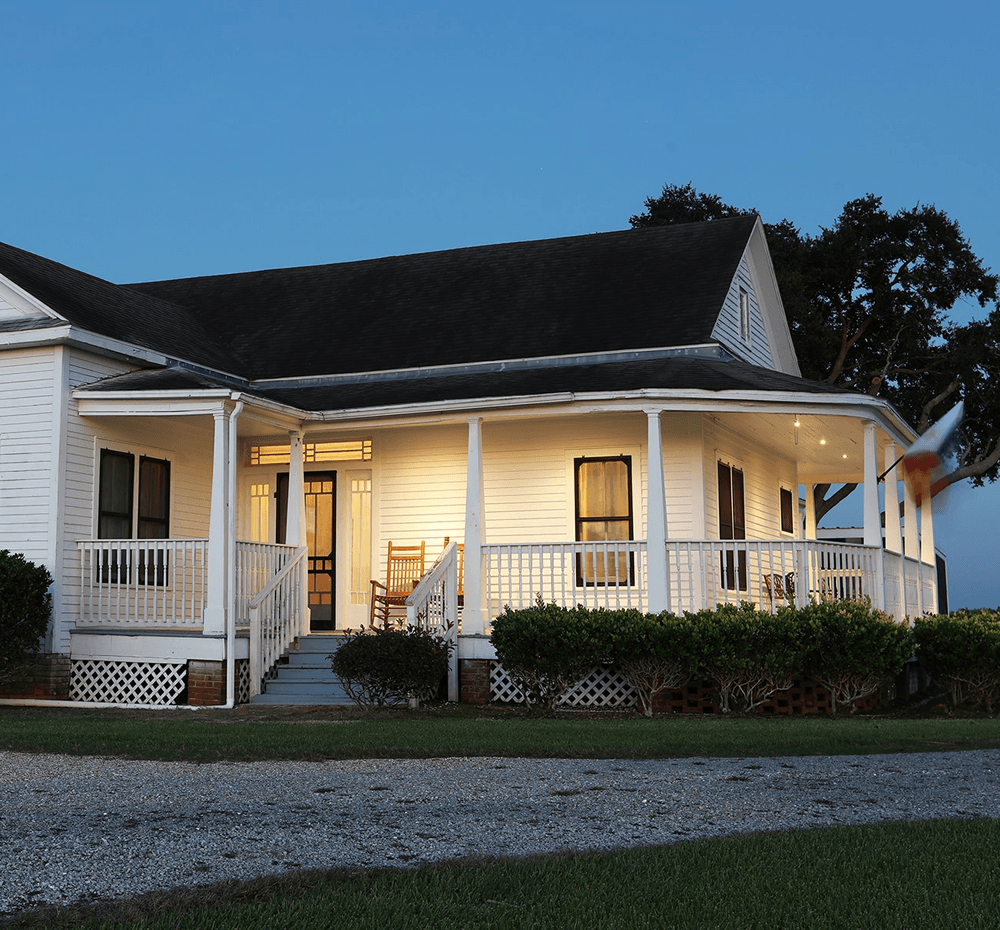 A charming white house with a welcoming porch and rocking chairs, set against a twilight sky.