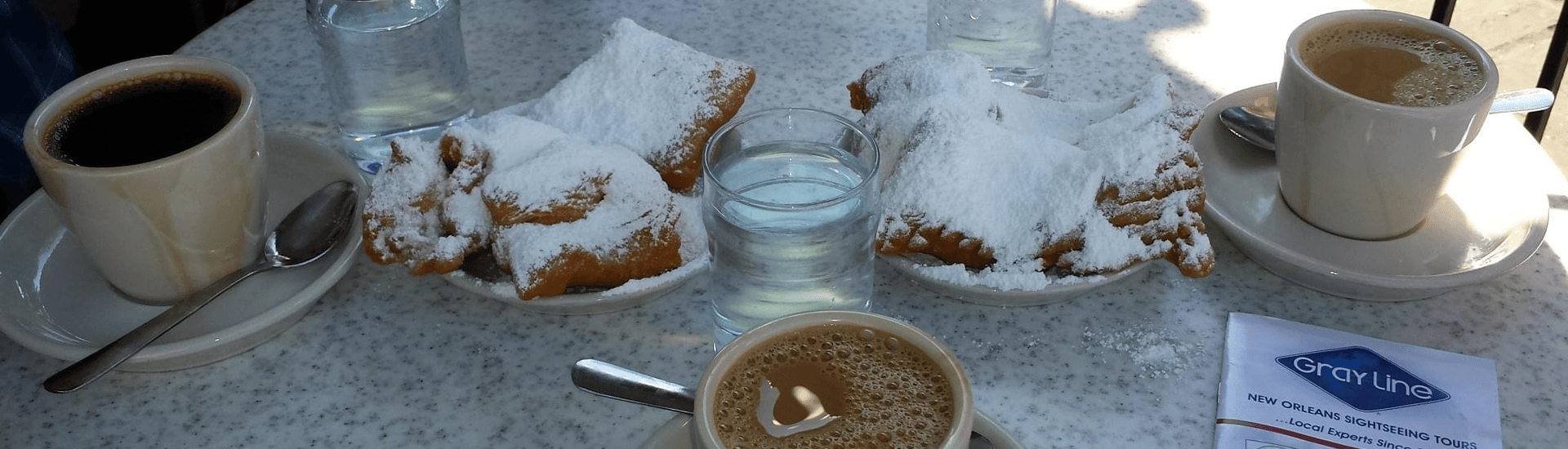 A table set with coffee, beignets dusted in powdered sugar, and glasses of water.