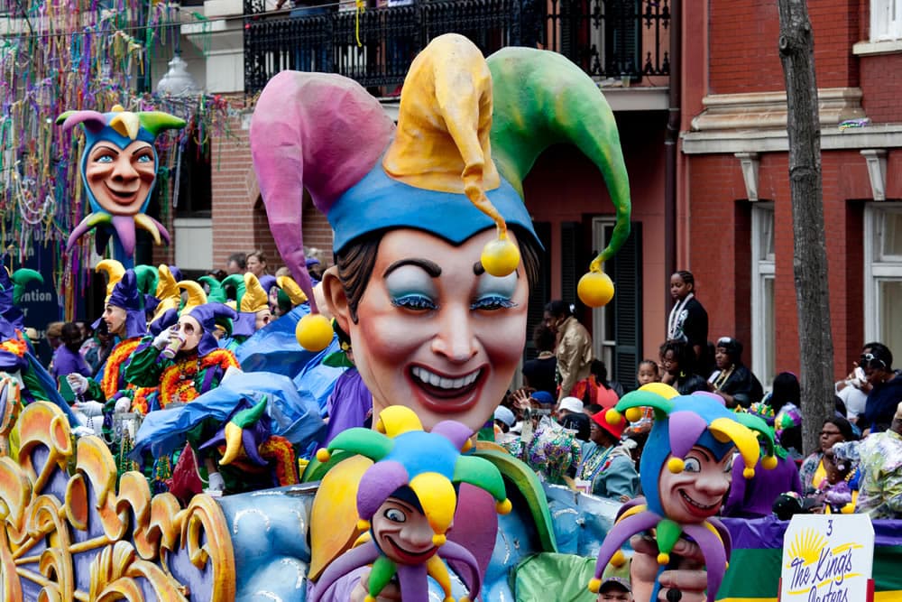A vibrant parade scene featuring colorful jester floats and participants in festive attire.