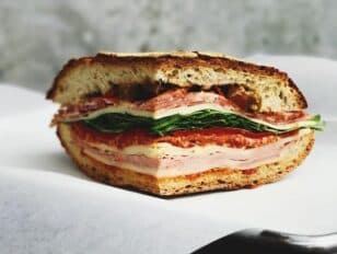 A cut sandwich with layers of meat, cheese, and greens on toasted bread.