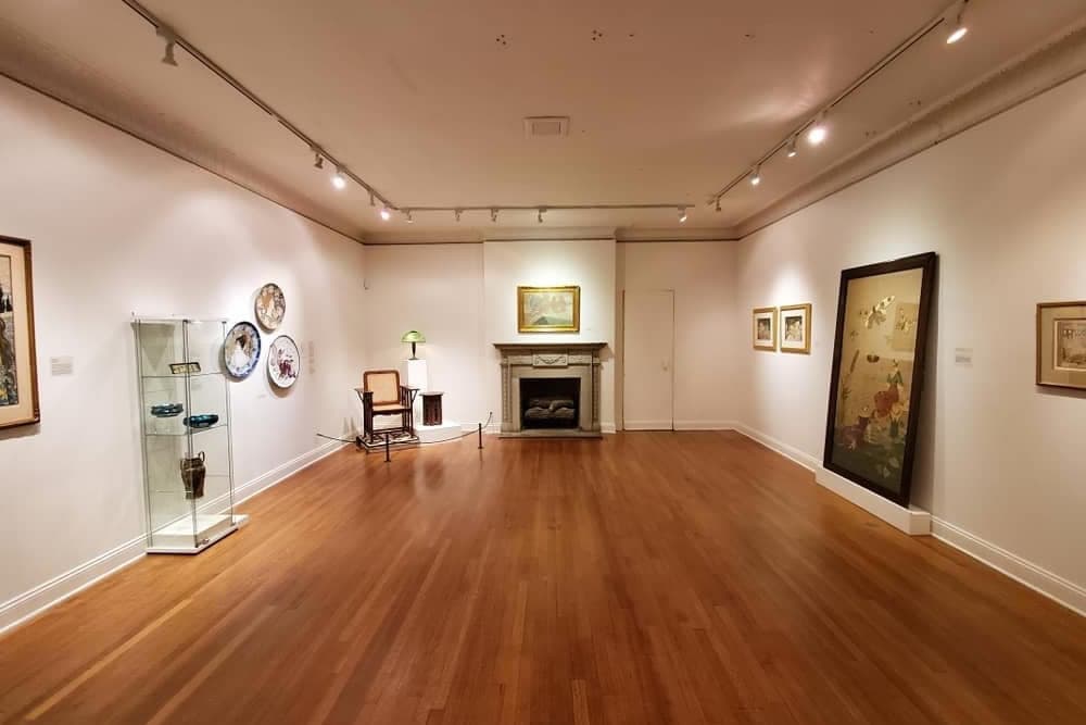 A spacious art gallery featuring framed artwork, decorative plates, and a chair near a fireplace.
