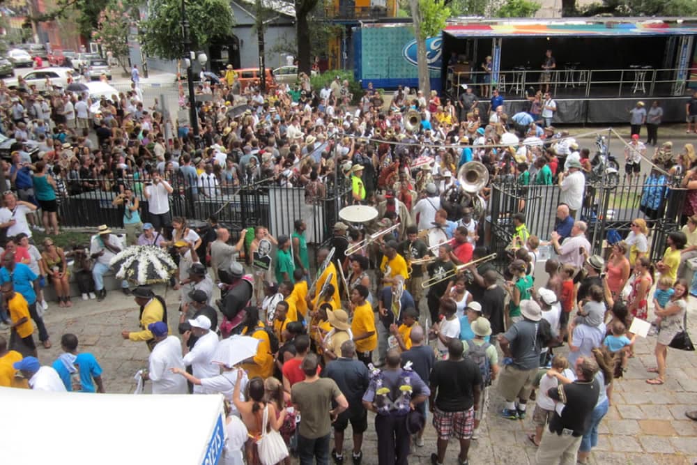 A lively crowd gathers for a street music performance, surrounded by musicians and festival activities.
