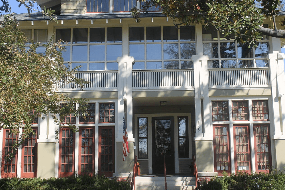 Front view of a two-story building with large windows and red accents, featuring a porch and American flag.