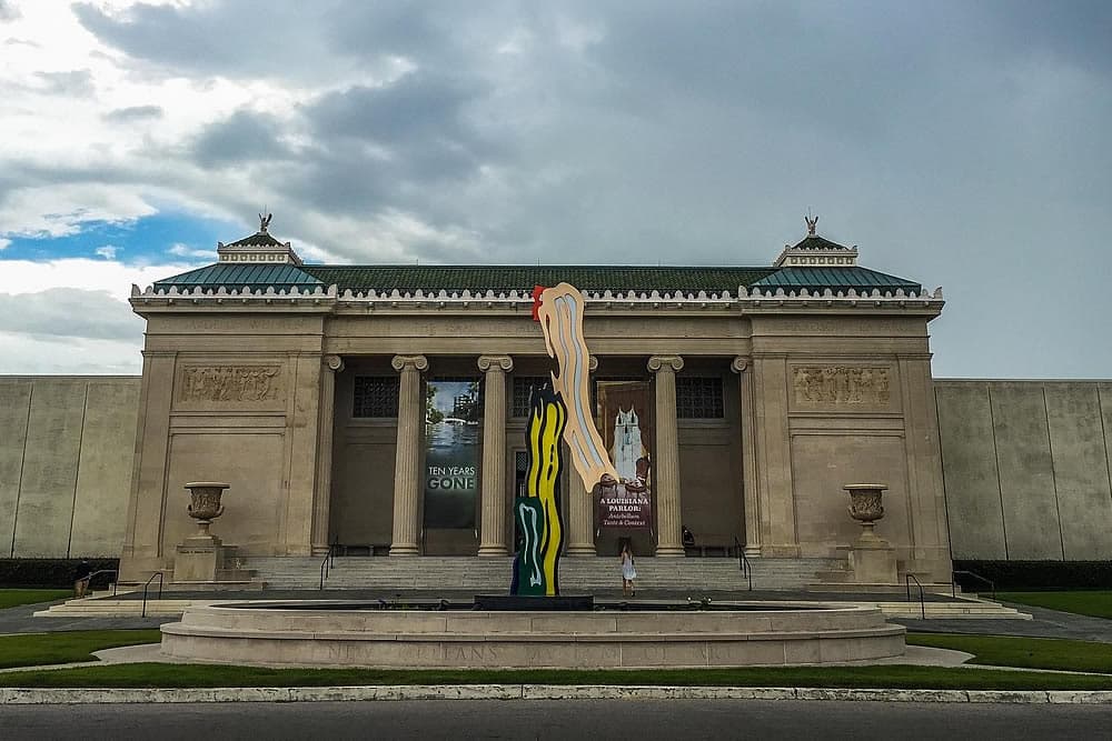 A colorful sculpture stands in front of a classic museum building under a cloudy sky.
