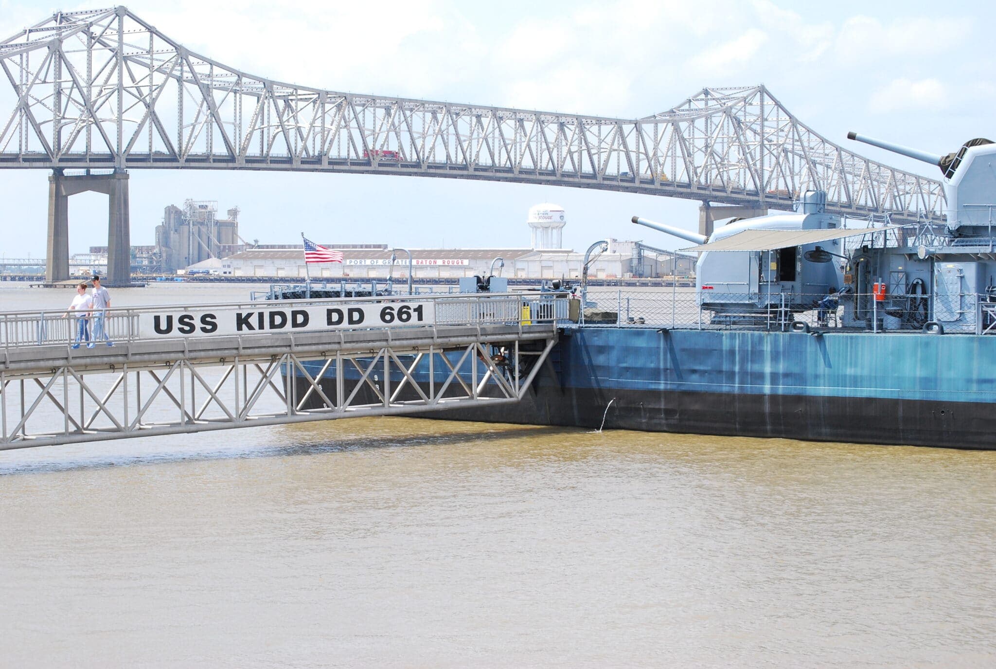 The USS Kidd DD 661 docked with a bridge and water in the foreground. The USS Kidd DD 661 docked with a bridge and water in the foreground.