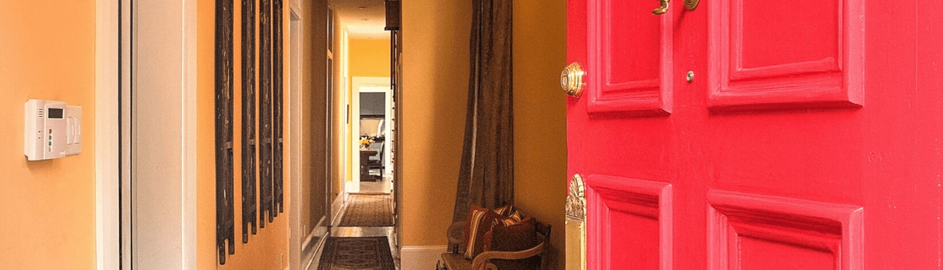 A bright red door opens into a warmly lit hallway with yellow walls and a glimpse of a room beyond.