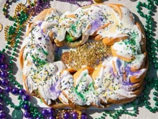 A colorful King Cake decorated with frosting and sprinkles, surrounded by Mardi Gras beads.