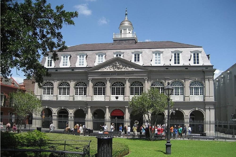 Historic building with arched windows and a dome, surrounded by trees and people.