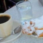 Cup of black coffee, glass of water, beignets with powdered sugar